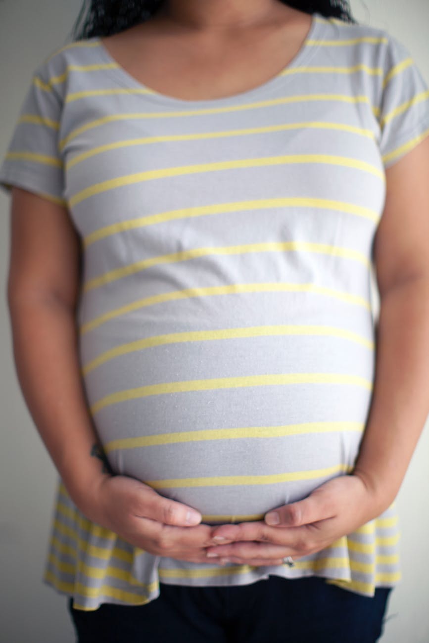 crop faceless pregnant woman touching belly with both hands