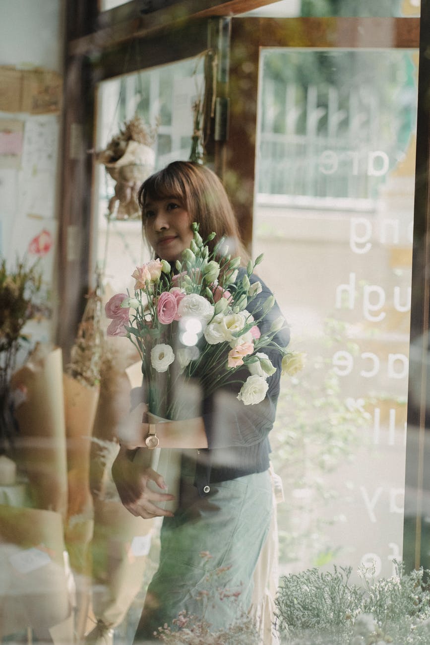 ethnic woman with bouquet of flowers walking into shop