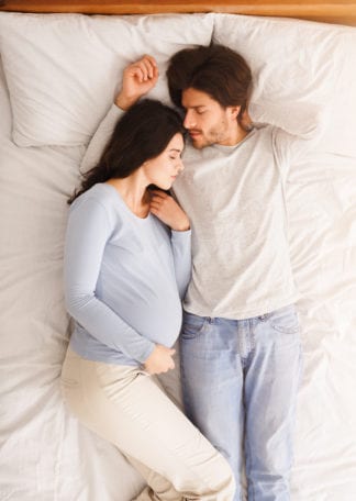 Pregnant couple sleeping together in comfortable bed